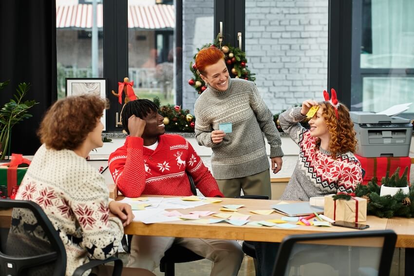 Work Christmas party ideas: 4 employees wearing Christmas-themed sweaters, playing a game