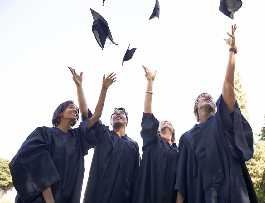 4 graduates throwing their graduation caps up into the air