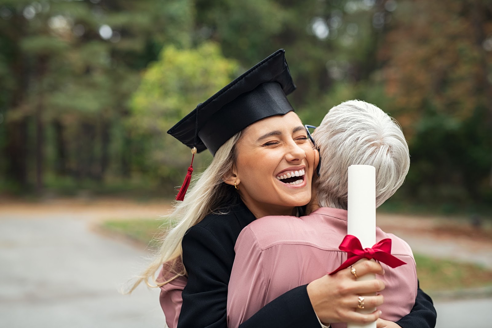 graduation card ideas: Smiling new graduate hugging her mother while holding her diploma
