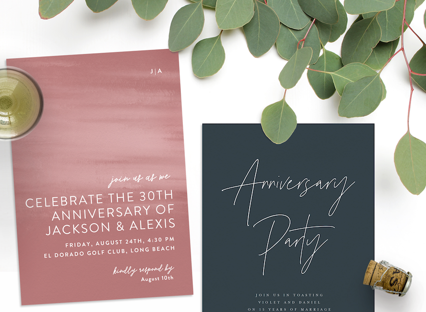 Two anniversary invitations with greenery, a glass of champagne, and a champagne cork