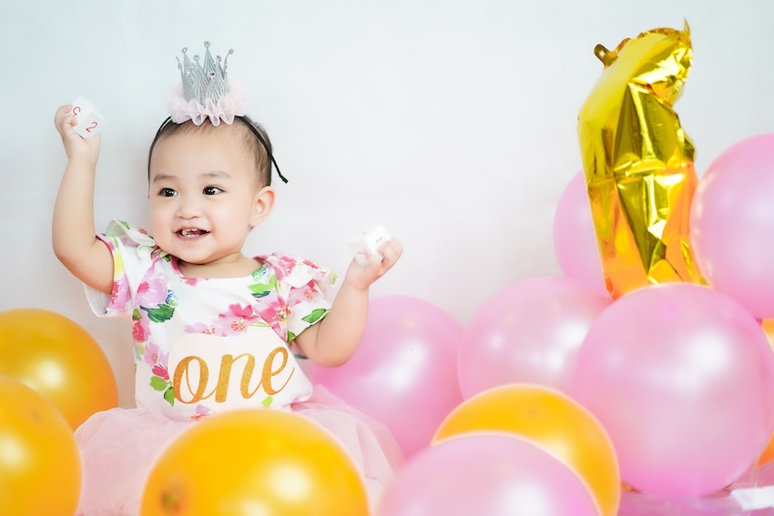 Girls first birthday theme: baby girl surrounded by yellow and pink balloons