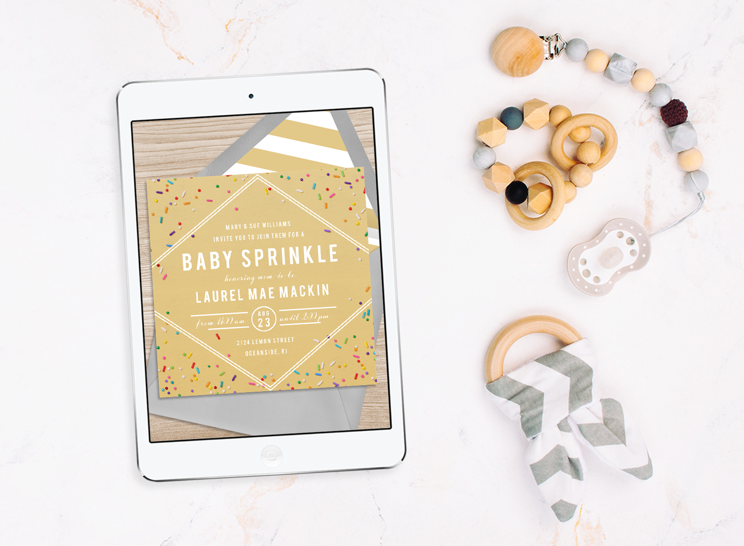 A digital baby sprinkle invitation on a tablet next to baby toys