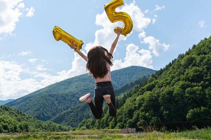 15th birthday ideas: back view of a girl jumping while holding golden number 15 balloons
