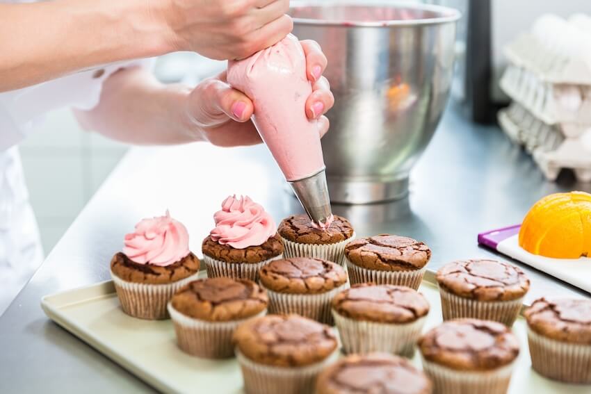 Baking birthday party: baker piping frosting onto some cupcakes