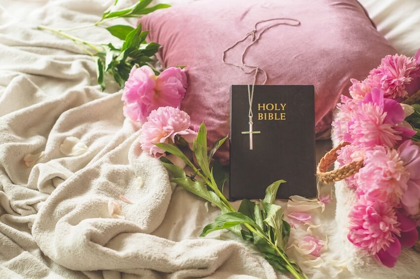 Spiritual happy birthday blessings: Holy Bible, pink flowers, and a cross necklace on a bed