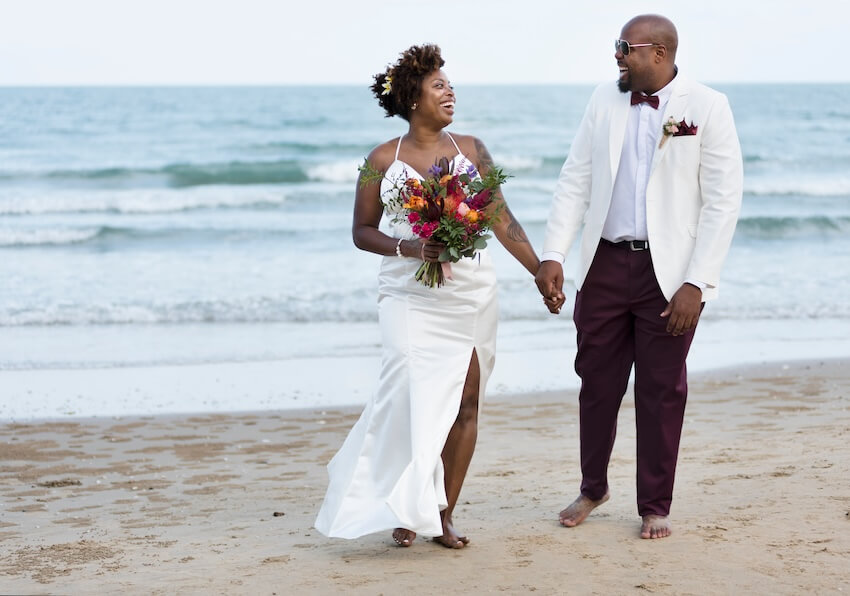 Bride and groom happily holding hands while walking at a beach