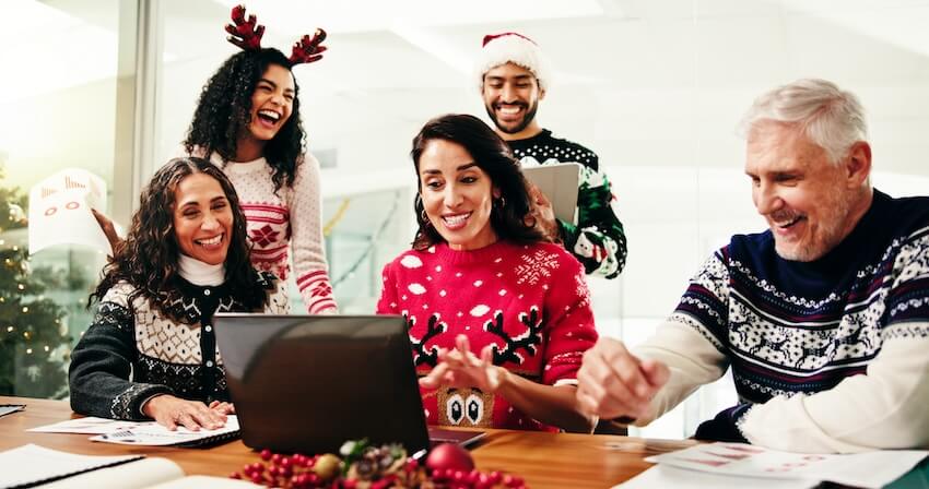 Business happy holidays message: colleagues wearing Christmas sweaters, looking at a laptop