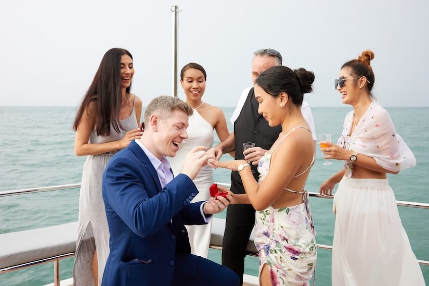 A couple getting engaged on a boat surrounded by friends