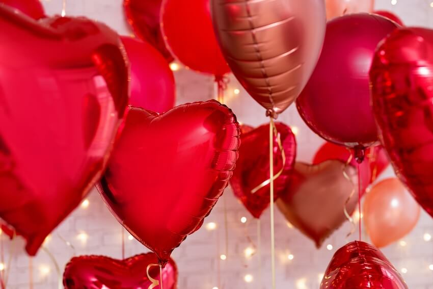 Floating heart-shaped balloons and string lights in the background