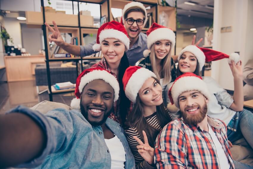 Holiday team building activities: friends wearing Santa hats while taking a groufie