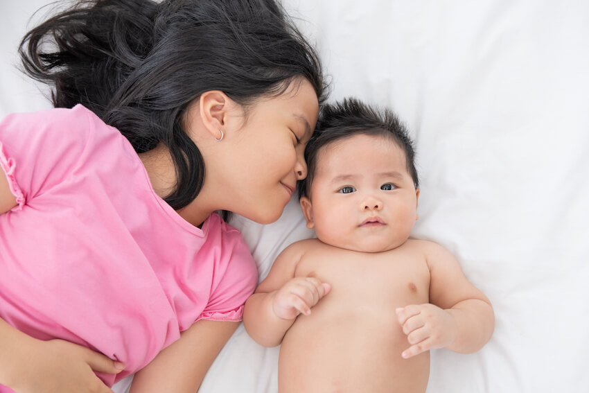 Big sister announcement: girl and a baby lying on a bed