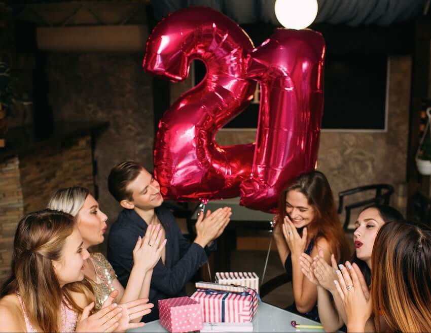 Group of friends clapping their hands, holding red number 21 balloons