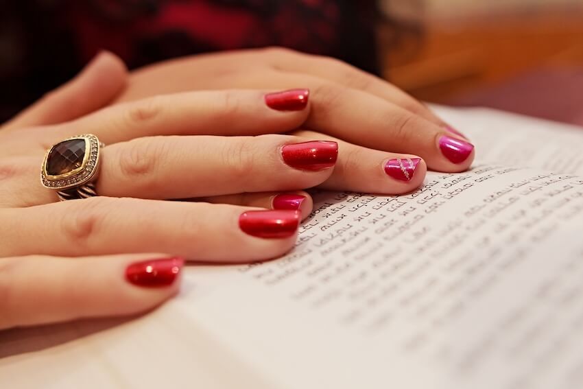 Bat Mitzvah invitations: hands of a woman with red nail polish resting on a book