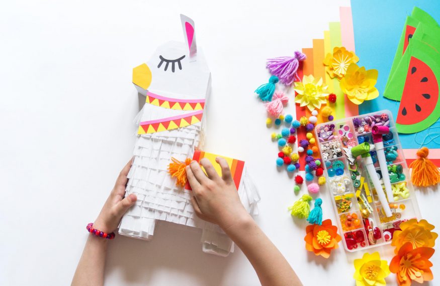 DIY party decorations: Person decorating a piñata on top of a white surface with decorating tools on the side