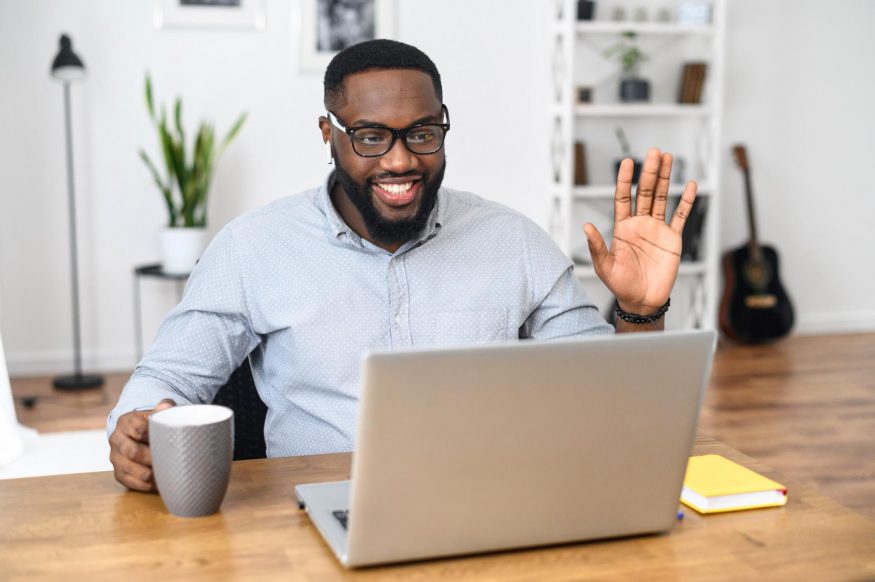 Remote team building activities: employee smiling and waving in front of his laptop