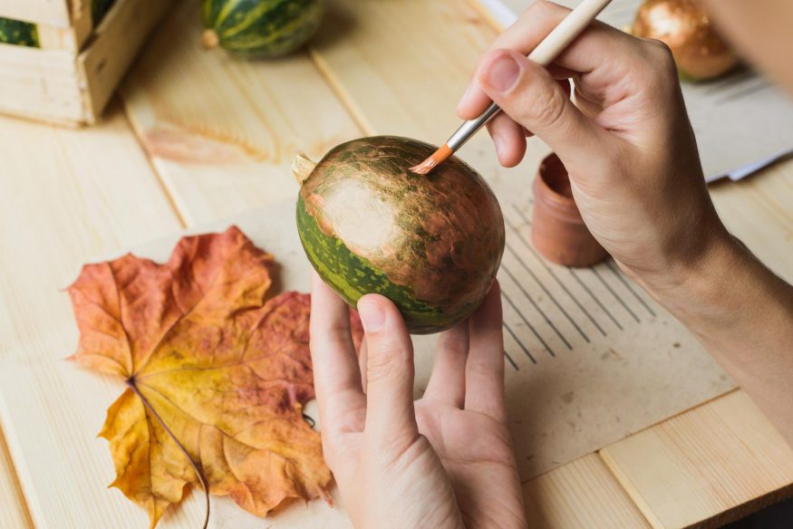 Person painting a small pumpkin