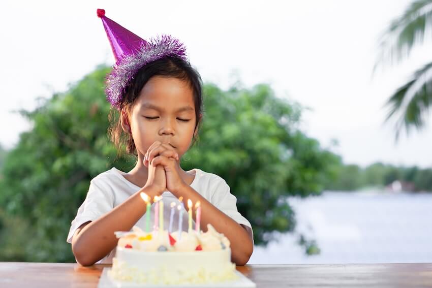 Spiritual happy birthday blessings: kid wearing a party hat while wishing in front of her cake