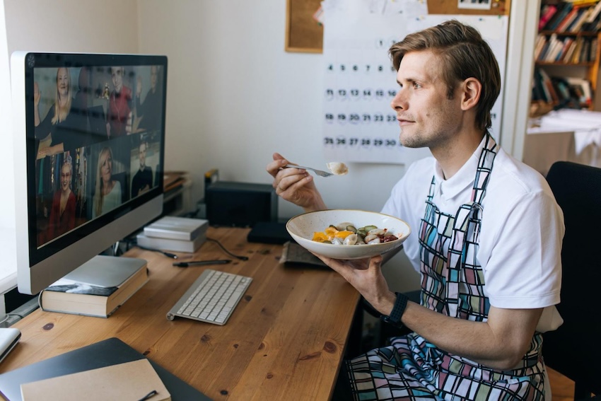 Man with an apron on, eating during an online meeting