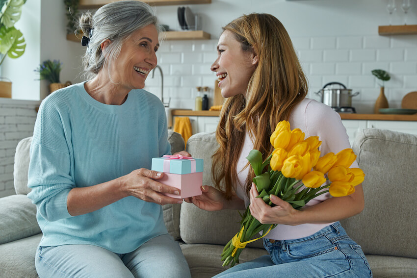 Happy birthday daughter: mother giving her daughter a gift and a bouquet of flowers