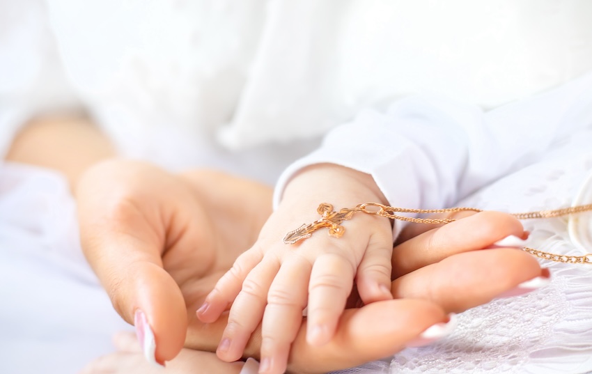 Mother holding her baby's hand with a cross necklace on top of it