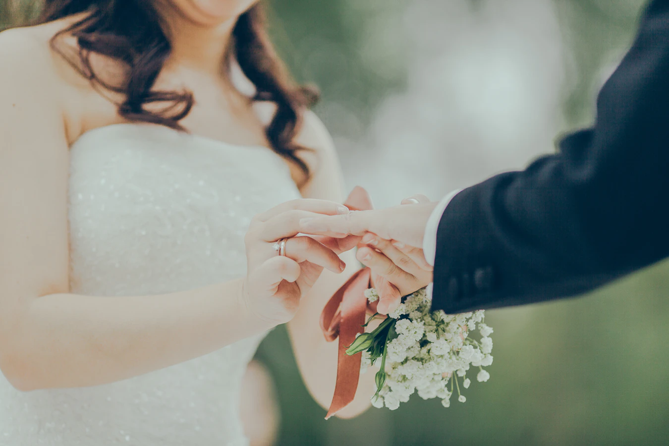 A bride puts a ring on a groom's finger