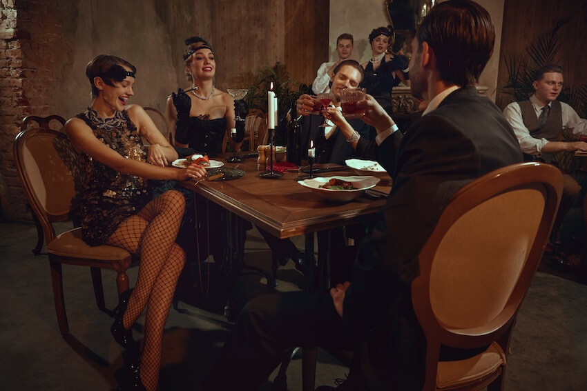Murder mystery party ideas: people drinking and eating at a vintage-themed dinner party