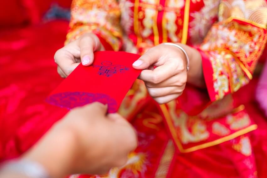 Asian wedding invitations: person handing a red envelope to another person