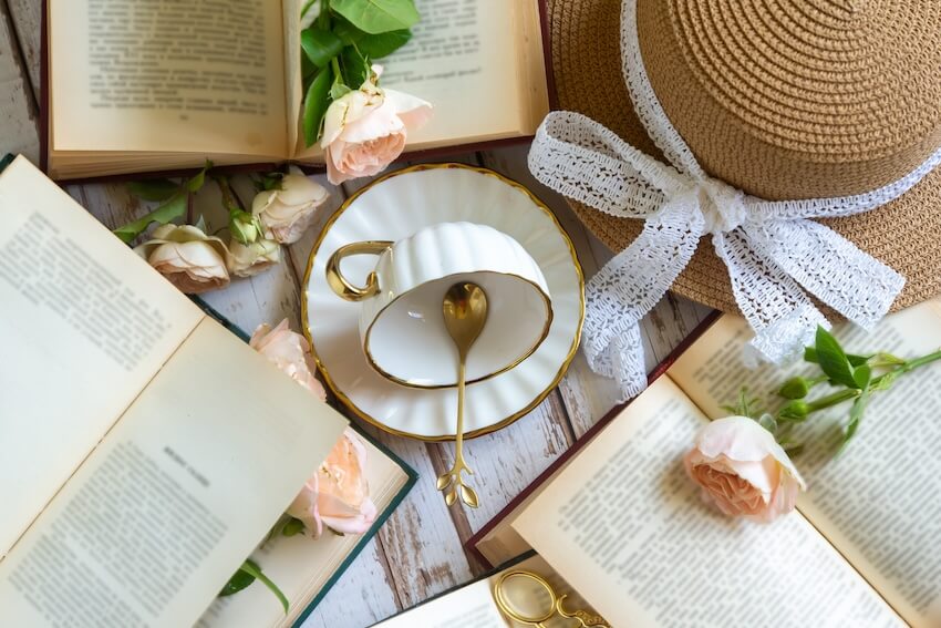 Porcelain cup and saucer, flowers, books, and a hat on a table