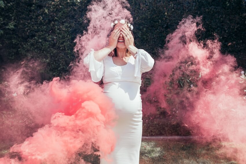 Baby reveal ideas: pregnant woman covering her eyes with her hands while pink smoke surrounds her