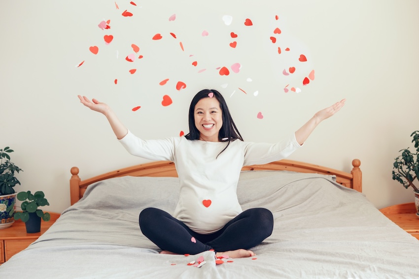 Valentine's Day pregnancy announcement: pregnant woman throwing small paper hearts up into the air