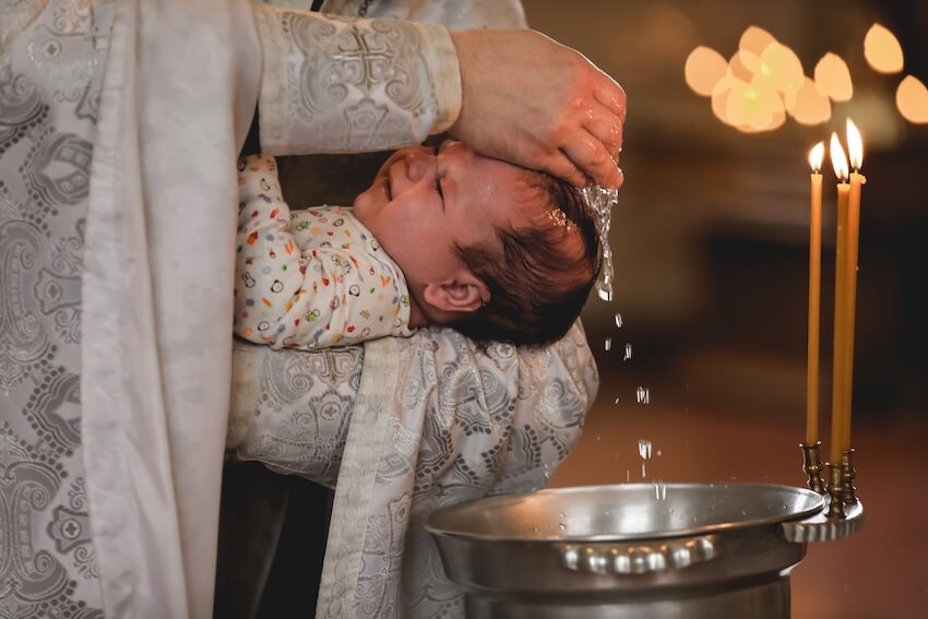 Congratulations words for baptism: priest baptizing a baby