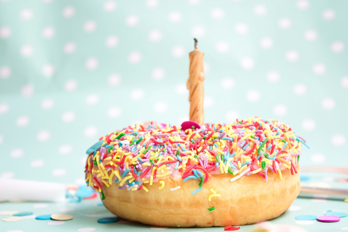 Birthday invitation wording: A sprinkled donut with a birthday candle