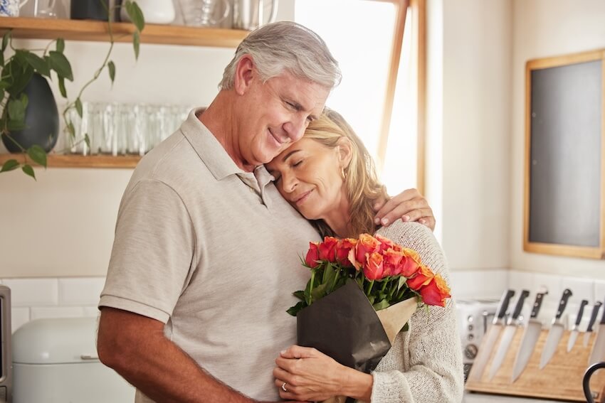 Senior couple hugging while holding a bouquet of flowers