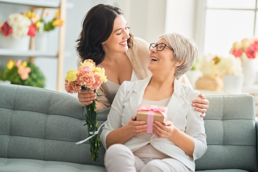 Happy mothers day blessings: woman giving her mother a gift and a bouquet